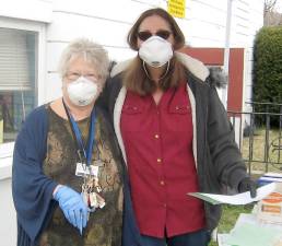 Masked pantry volunteers Judy Miller (left) and Doreen Edwards safely distribute supplies.