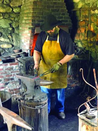 The Waterloo Village blacksmith hammers out a nail.