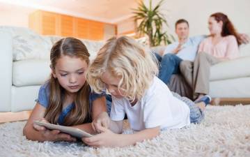 Siblings using tablet together on the living room floor