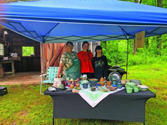 Kathleen Nolan of Pequest Pottery and her grandchildren pose behind a table holding some of her work.