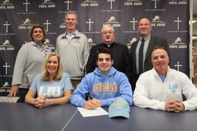 Pope John senior Justin Hertlein signs his National Letter of Intent to continue his academic and football careers at Long Island University on Wednesday, with his mother, Denise, and father, John at his side. Standing in back are Pope John Athletic Director Mia Gavan, head coach Brian Carlson, President Rev. Msgr. Kieran McHugh, and Principal Gene Emering.