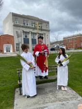 Reverend Canon Father Robert Griner conducts the service a-top a bench, in the now, in the middle of the Newton Green on Palm Sunday.