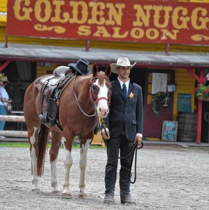 Cowboy Gabe Wellington stands next to Ranger carrying an empty saddle, boots reversed in the stirrups and Robert ‘Pony Bob’ Erven’s hat on the pommel. This horse, who joined Wild West City this season, was named for Erven’s favorite quarterhorse. (Photo by Jane Primerano)