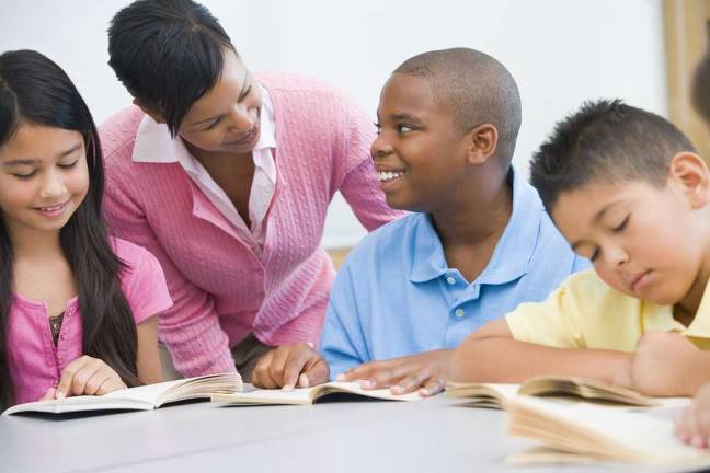 Students in class reading with teacher helping (selective focus)