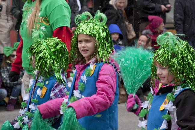 Members of the Girl Scouts march in colorful garb and shiny green wigs.